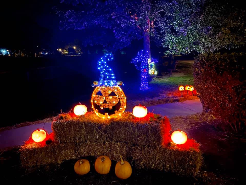 Halloween-themed display with illuminated jack-o'-lanterns, hay bales, and blue-lit decorations at night.