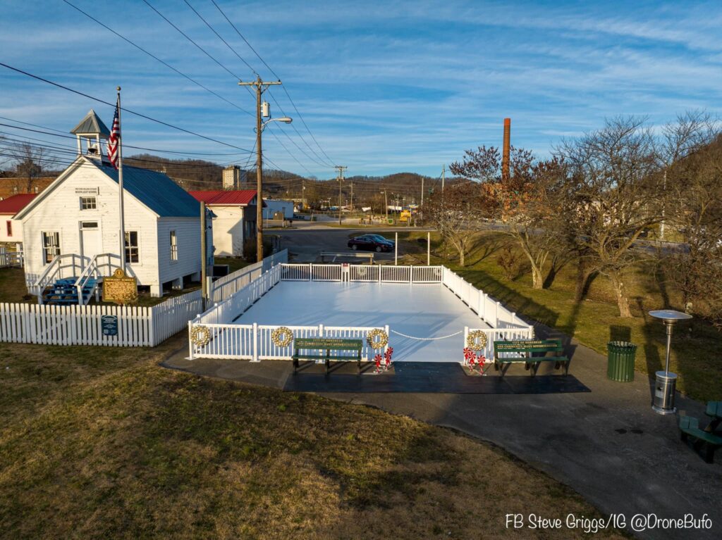 An outdoor ice rink surrounded by white fencing, adjacent to a small white building with a blue roof and an American flag.