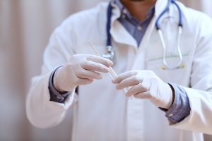 A healthcare professional in a lab coat and gloves holds a test swab and tube.