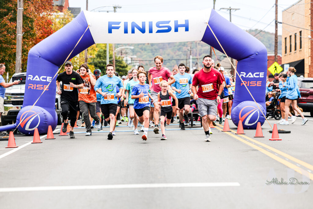 Runners cross a finish line under a blue arch in a road race event.