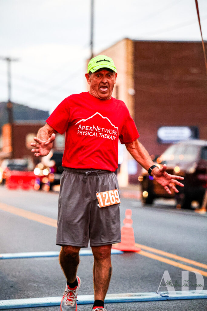 Runner wearing a red shirt and gray shorts participates in a road race, with an orange headband and race number 1269.