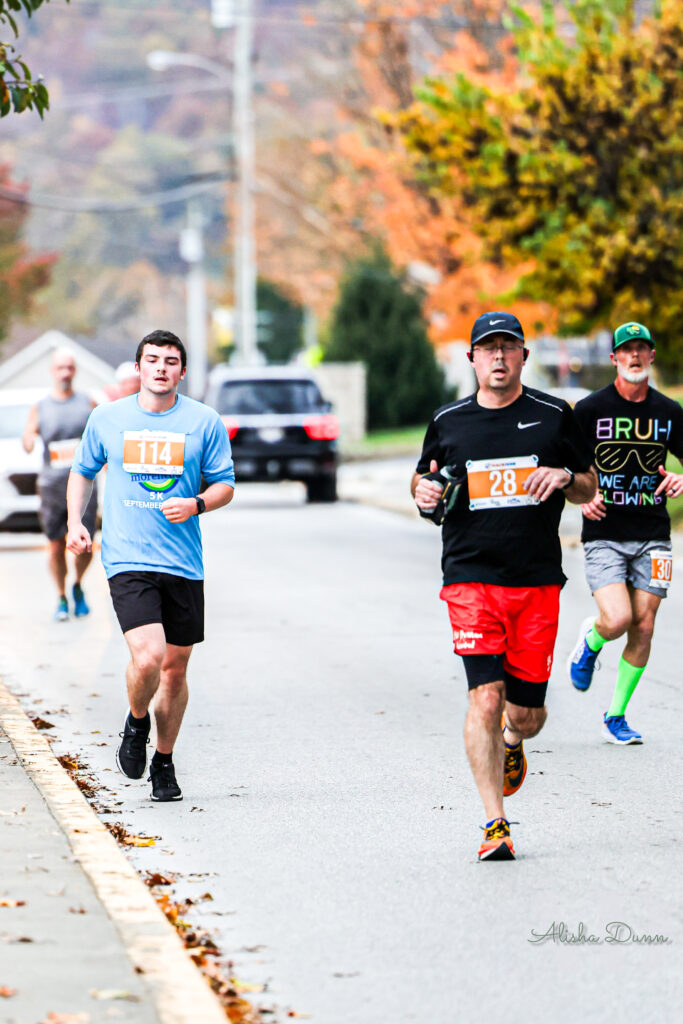 Runners participating in a road race on a tree-lined street during autumn.