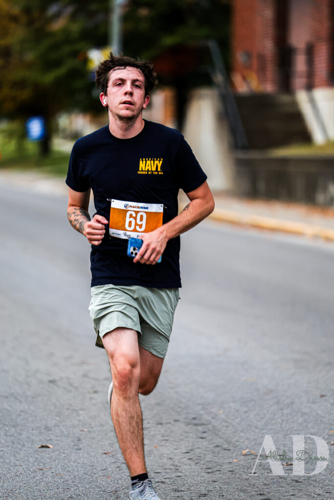 Runner on a street wearing a navy shirt and bib number 69, with buildings in the background.