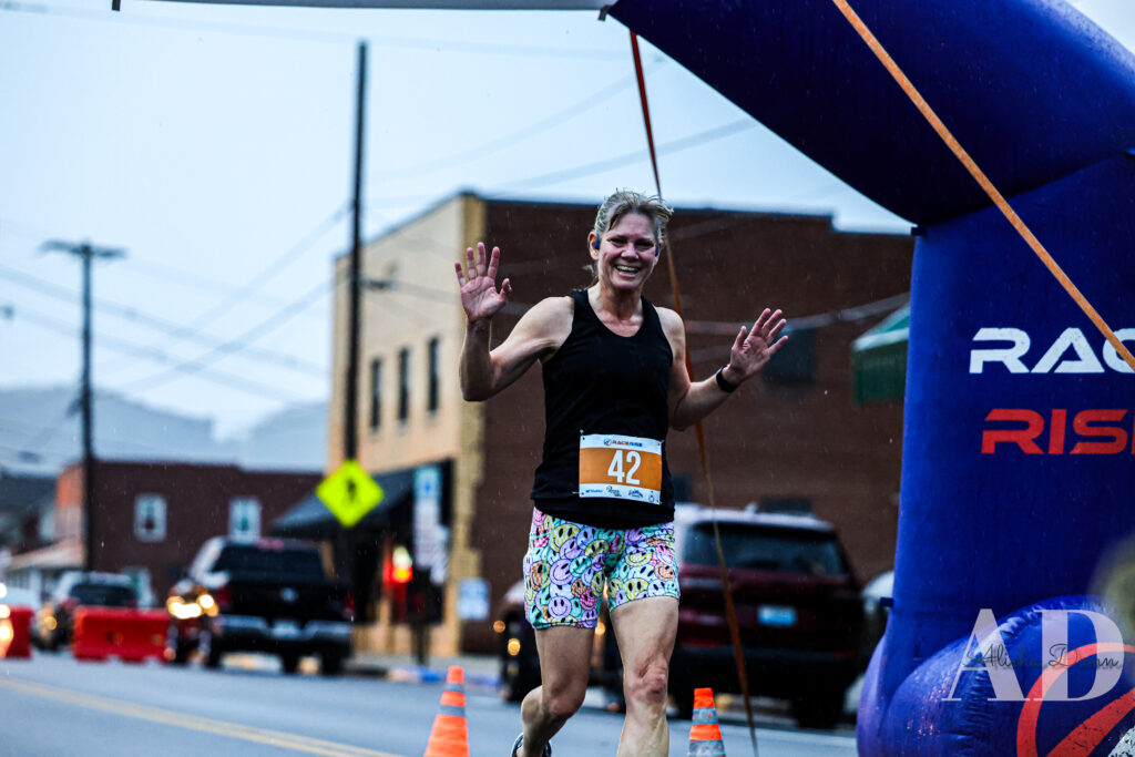 Runner wearing race number 42 crosses the finish line beneath an inflatable arch on a city street.