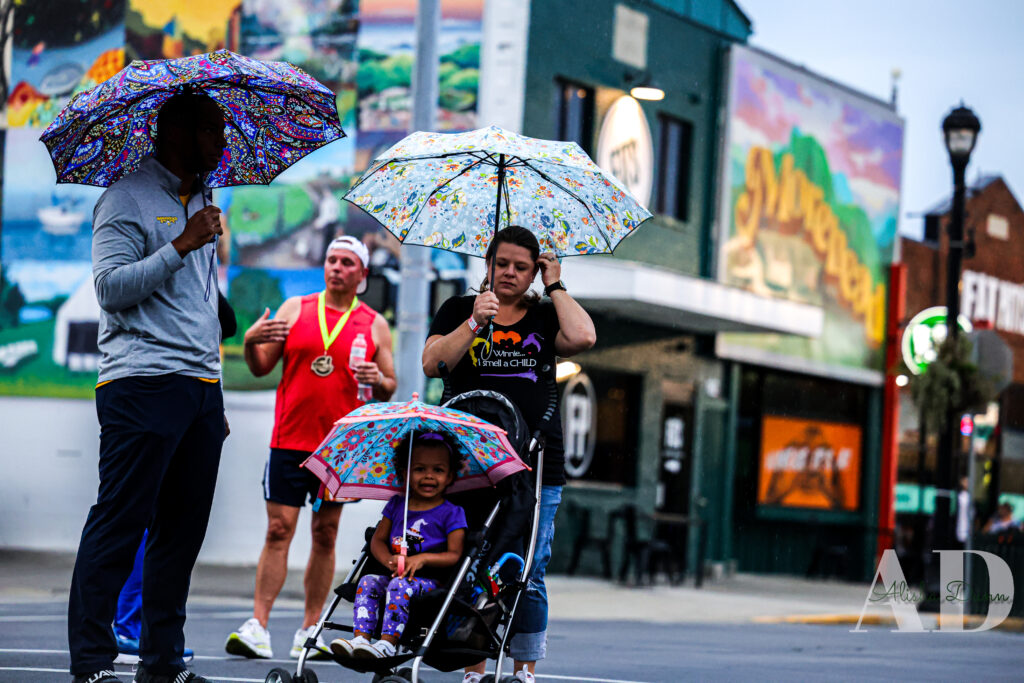 Three adults and a child with umbrellas stand on a street near a building with colorful murals.