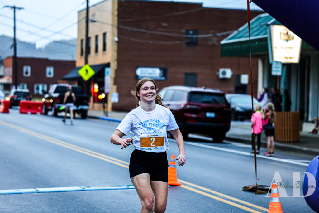 Runner crossing a finish line in a street race, wearing a bib number 2, with traffic cones and spectators in the background.