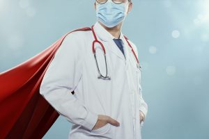 'Healthcare professional wearing a white coat, stethoscope, face mask, and a red superhero cape.'